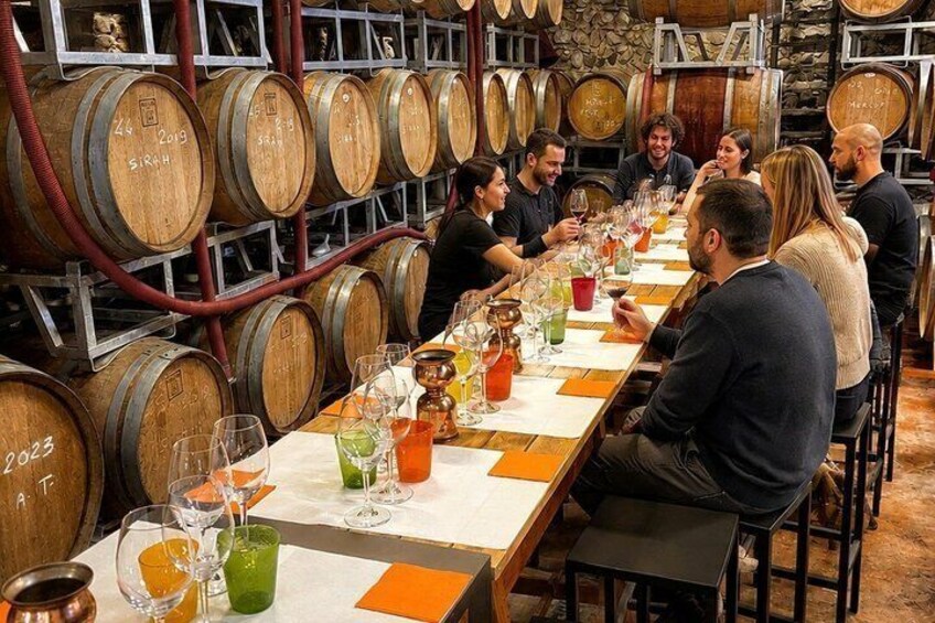 A group of people seated at a long table in a cellar with wooden barrels. 1