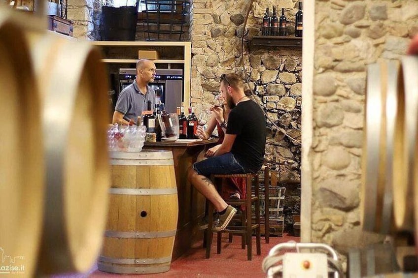 A man sitting at a table in a rustic bar setting with wooden barrels and stone walls. 3