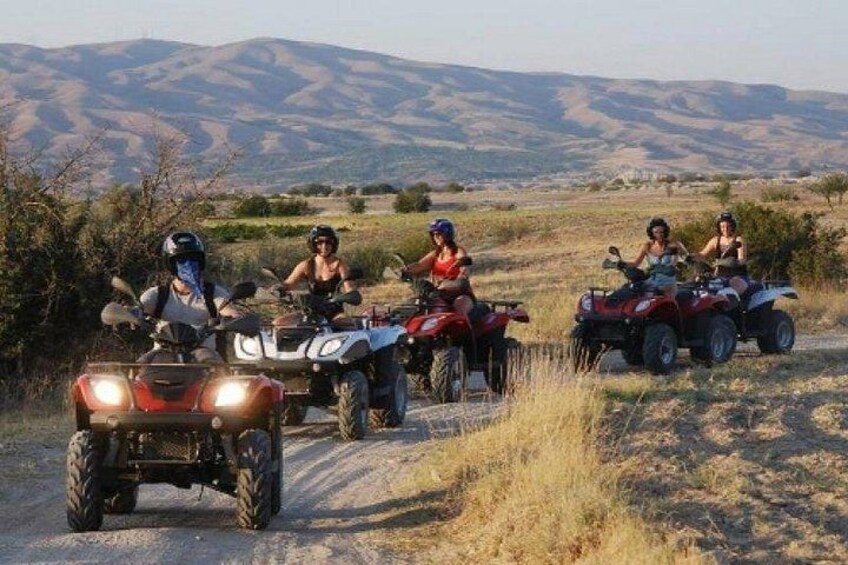 Quatre personnes conduisent des quads sur un chemin de terre, avec un paysage montagneux en arrière-plan. 1