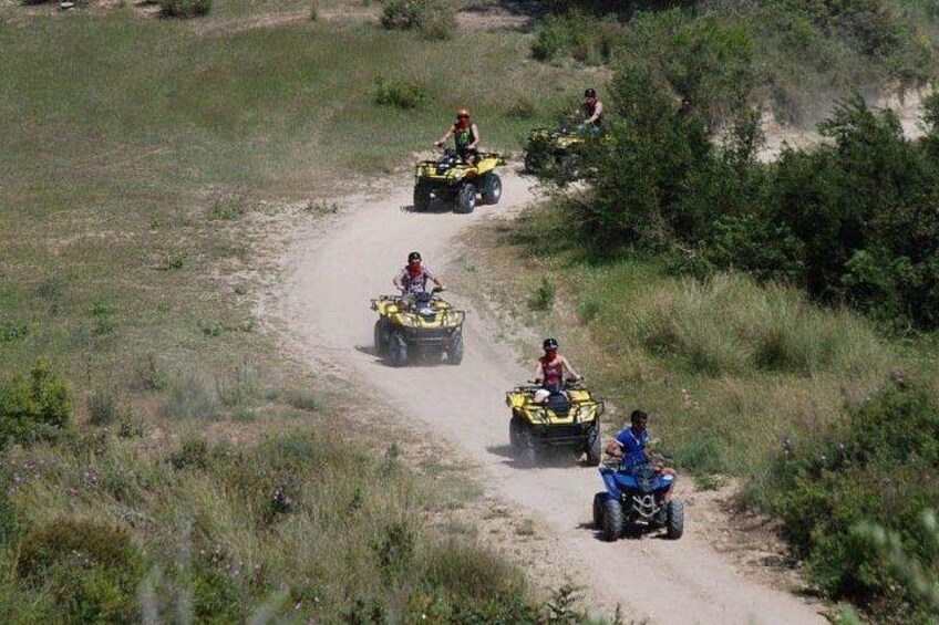 Quatre personnes conduisent des quads sur un chemin de terre, entourés d’herbe et de buissons. 5