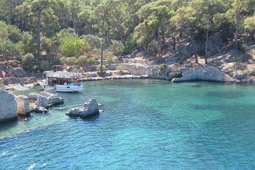 A boat on a turquoise sea with rocky outcrops and dense trees in the background. 3