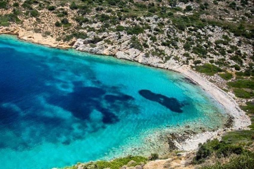A coastal landscape with clear turquoise waters, rocky shoreline, and sparse vegetation. 3
