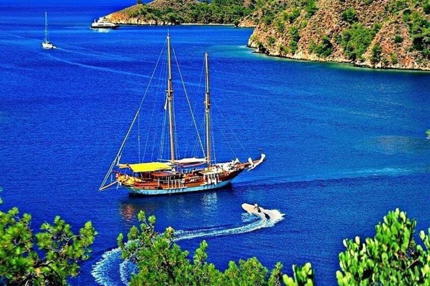 A sailboat on a calm sea with a small motorboat nearby, surrounded by lush greenery and rocky terrain. 4