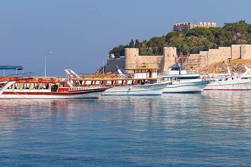 A harbor with several boats, a historic fort, and a hill with buildings. 2