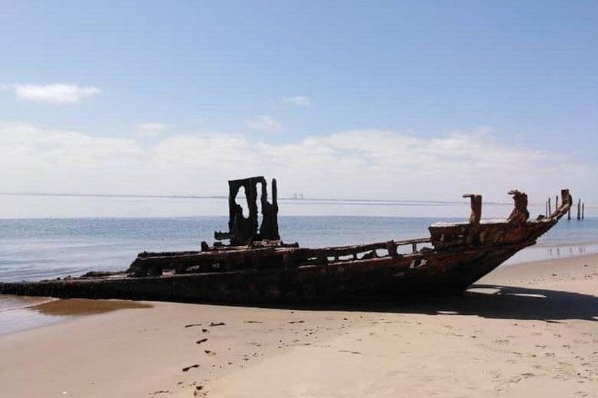 A rusted shipwreck on a sandy beach with calm water in the background. 3