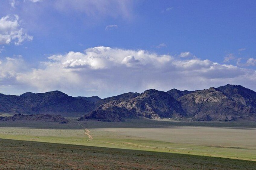 A vast open field with distant mountains under a partly cloudy sky. 3