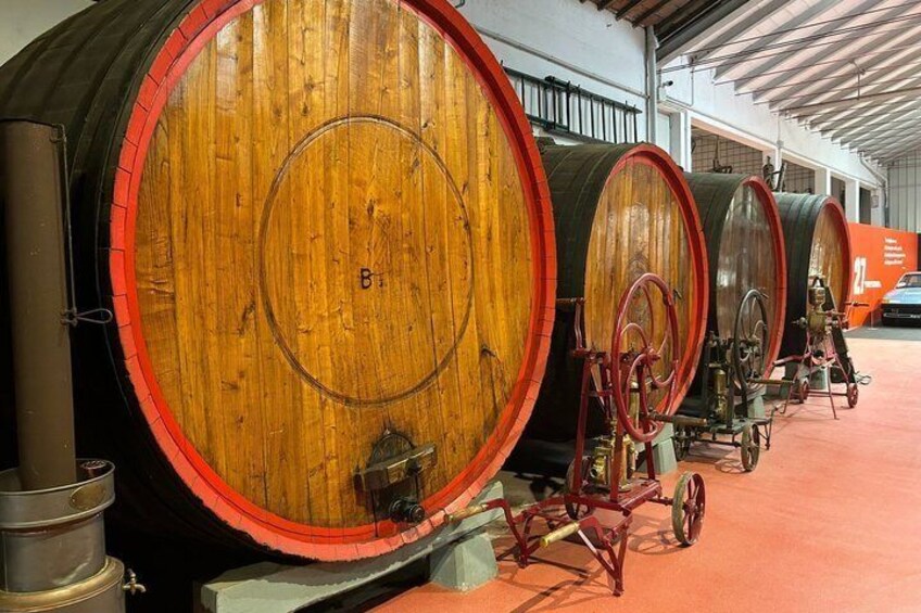 Wooden barrels with metal hoops, arranged in a row inside a building. 2