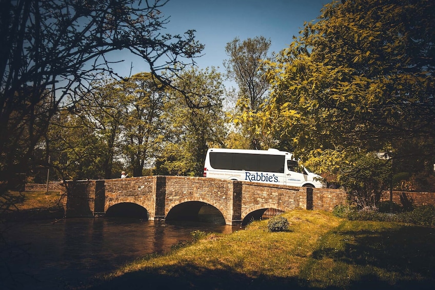 A white tour bus parked on a stone bridge over a river. 3
