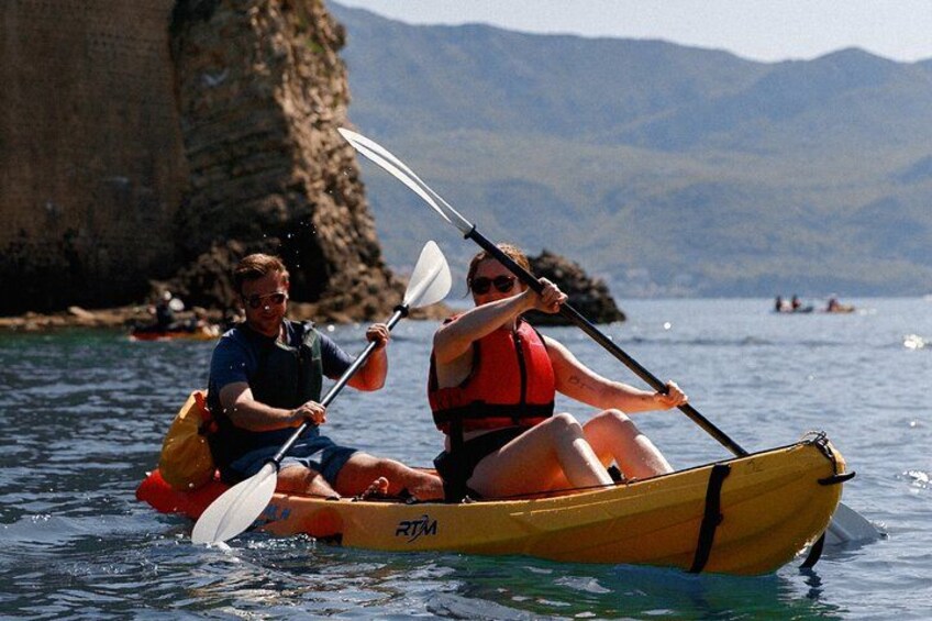 Budva Bay Kayak & SUP Tour to Coastal Caves – couple paddling an orange tandem kayak with mountain backdrop in Budva Bay 2