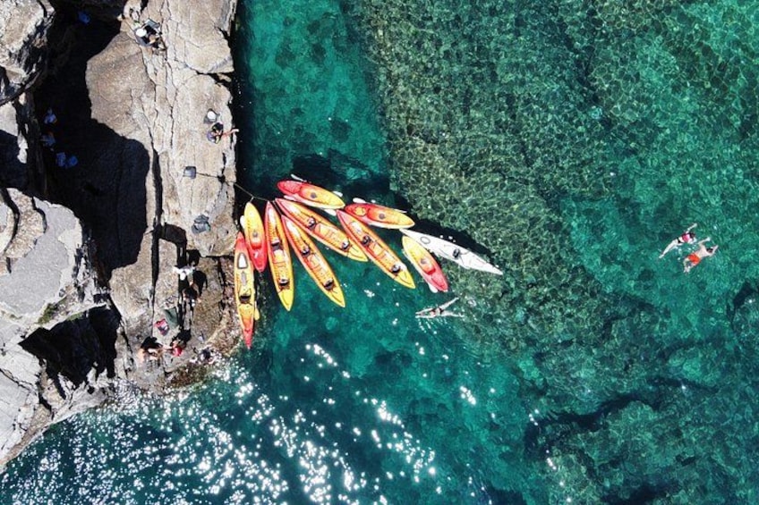 Une zone côtière où l’on peut voir des kayaks alignés sur la plage, une eau turquoise et limpide, et des falaises rocheuses. 3