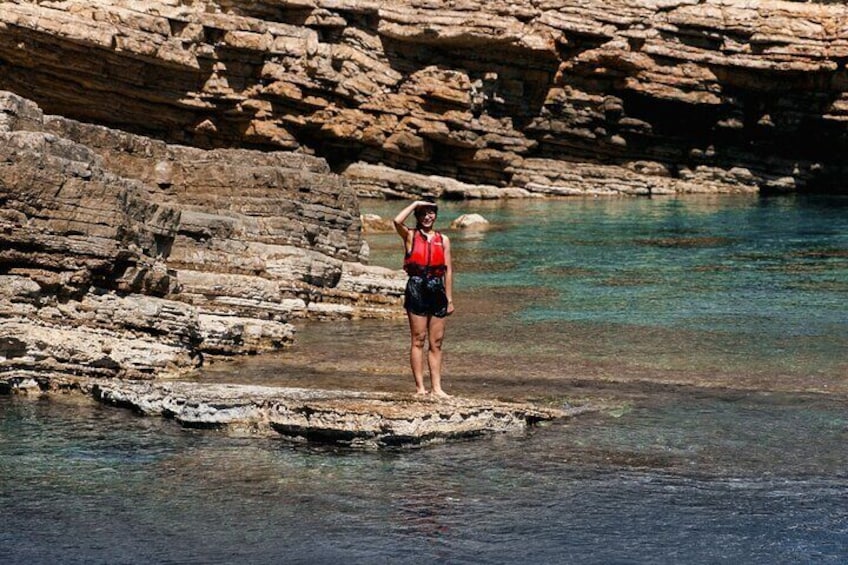 A person standing on a rock formation in a body of water with clear water and rocky cliffs in the background. 4