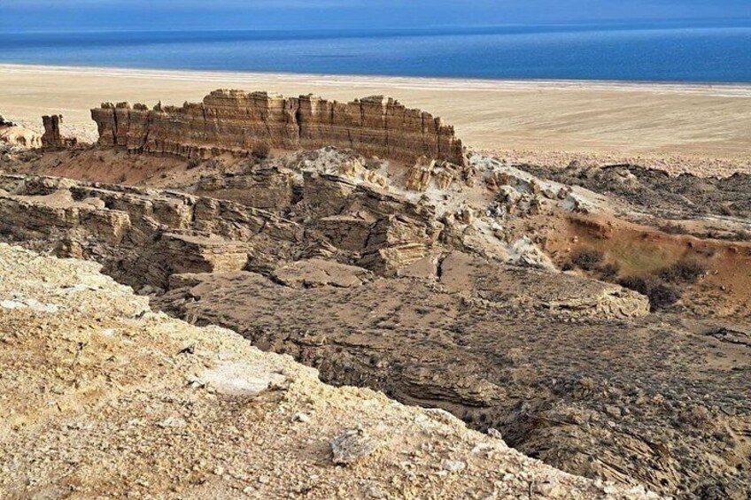 A rocky landscape with layered sedimentary rock formations and a distant view of the ocean. 3