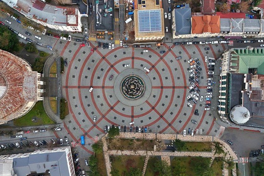 Vista aérea de una glorieta con carriles concéntricos, rodeada de edificios y coches aparcados. 1