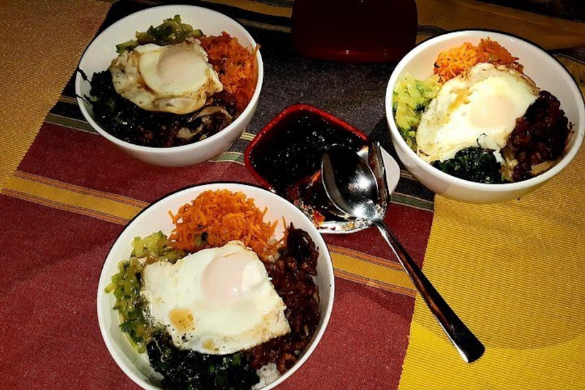 Tres tazones de comida con un huevo pochado encima, sobre una mesa con mantel a rayas. 5