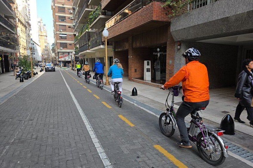 A city street with cyclists, buildings, and a parked car. 4