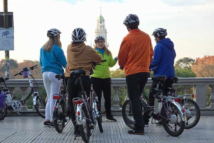 A group of cyclists on a bridge with bicycles and a clock tower in the background. 3