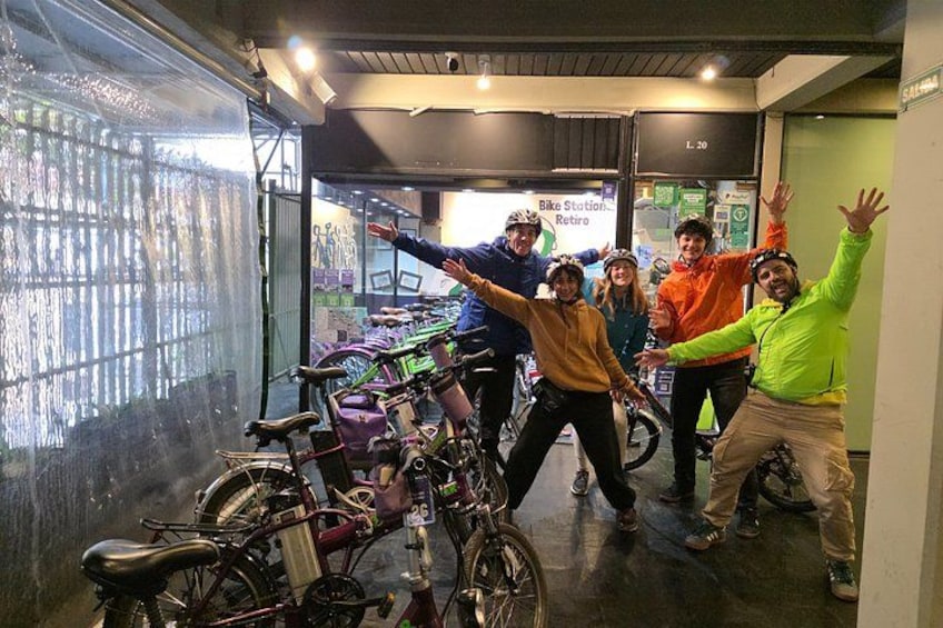 A group of people posing with bicycles in an indoor setting with a glass wall and a sign that reads 'Bike Station Retire.' 2
