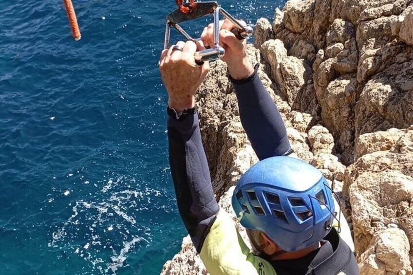Une personne portant un casque bleu et une veste jaune, tenant un appareil photo, se tient debout sur une falaise rocheuse au bord de la mer. 3