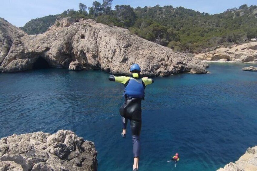 Une personne vêtue d’un gilet de sauvetage bleu et d’un casque, sautant d’une falaise rocheuse dans l’eau. 2
