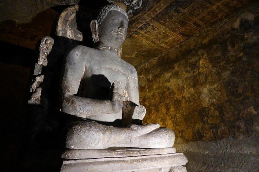 En stenskulptur som föreställer en sittande person, placerad i en grotta. 3