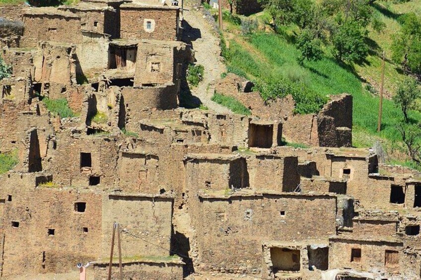 Un ensemble de constructions anciennes en briques de terre, dotées de nombreuses fenêtres et de plusieurs portes, et entouré d’une colline verdoyante. 3