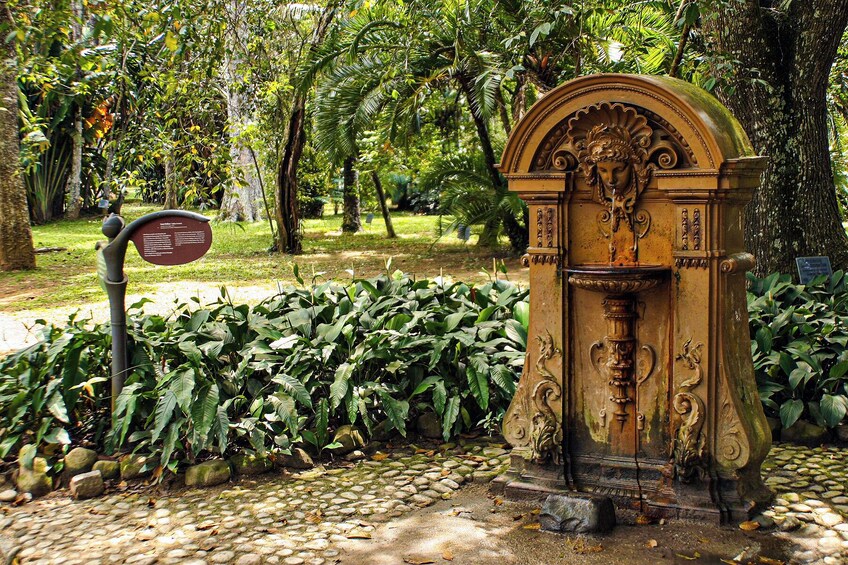 A stone fountain with intricate carvings, surrounded by lush greenery and a stone pathway. 3