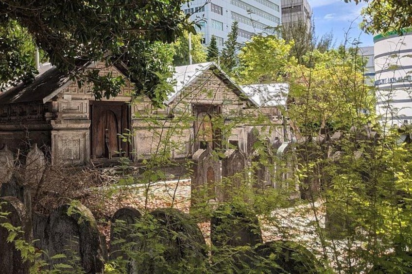 A cemetery with stone headstones, surrounded by trees and buildings. 2
