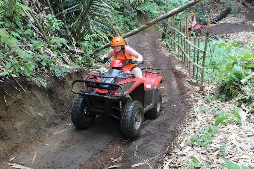 A person riding an ATV on a muddy path surrounded by dense vegetation. 3