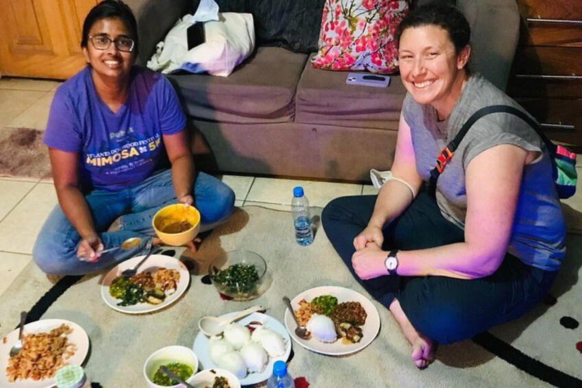 Two people sitting on the floor with plates of food in front of them. 1