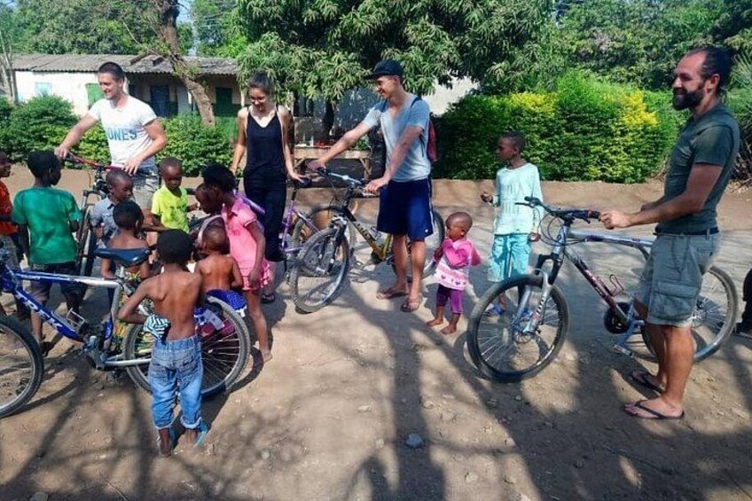Un grupo de personas, entre ellas niños y adultos, reunidas alrededor de bicicletas en un entorno al aire libre con árboles y un edificio al fondo. 1