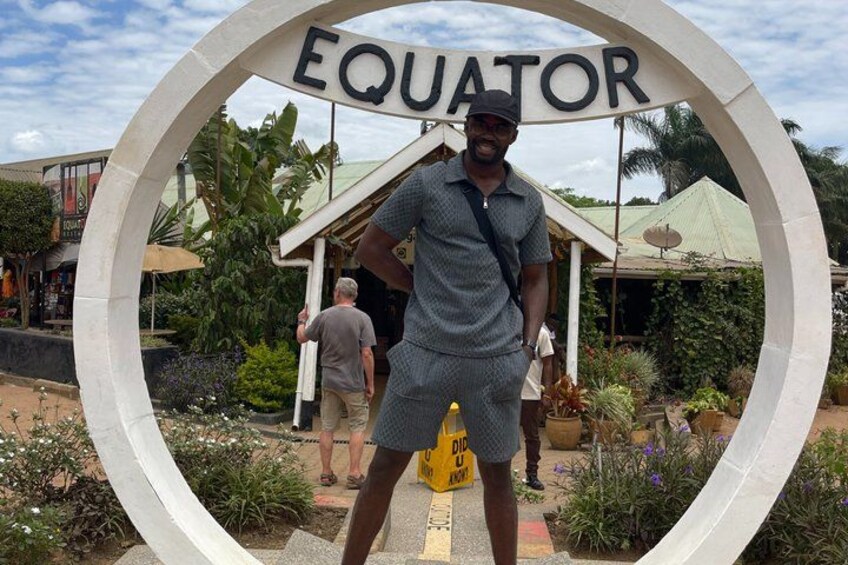 Un uomo in piedi di fronte a un grande cartello circolare con la scritta 'EQUATOR'. 3