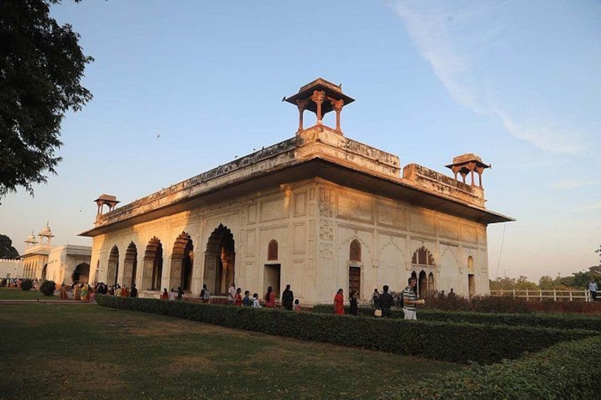 A large, historic building with arched windows and a central tower, surrounded by a well-maintained lawn and a few people. 3