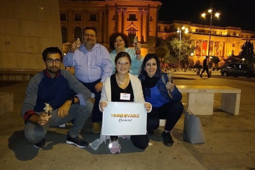 A group of people posing with a sign in front of a building at night. 4