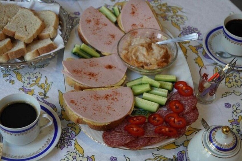 A table with sliced ham, cucumbers, cherry tomatoes, bread, and a bowl of dip. 2