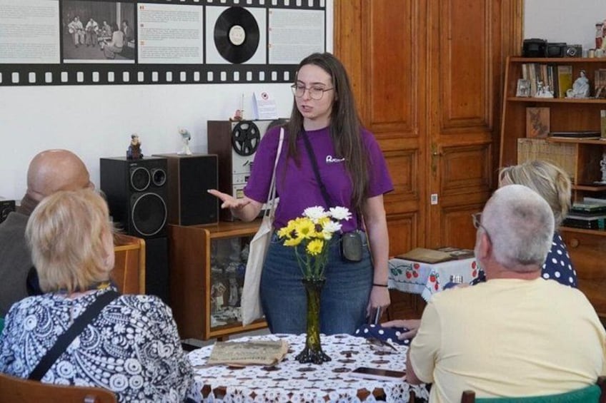 A woman in a purple shirt presenting to an audience seated at a table with a floral centerpiece. 3