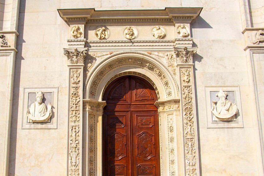 Una entrada imponente con una puerta de madera grande, tallas intrincadas y estatuas a ambos lados. 2