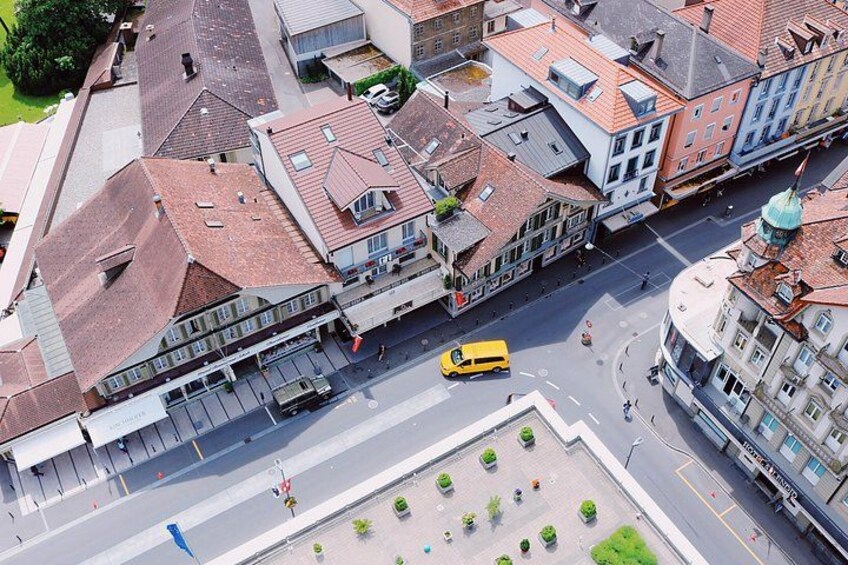 An aerial view of a city street with buildings, a yellow bus, and a roundabout. 2