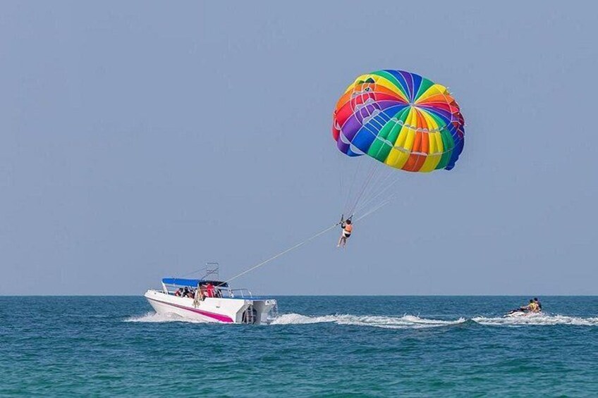 A parasailer with a colorful parachute over the ocean, a speedboat, and another person wakeboarding. 3