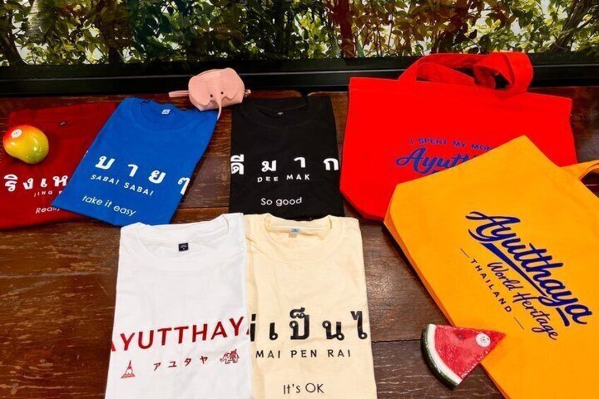 A variety of clothing items and bags with Thai text, placed on a wooden surface. 5