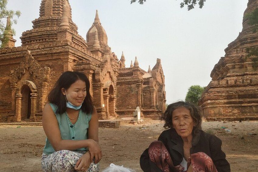 Two people sitting in front of a large, ancient brick temple with multiple spires. 5