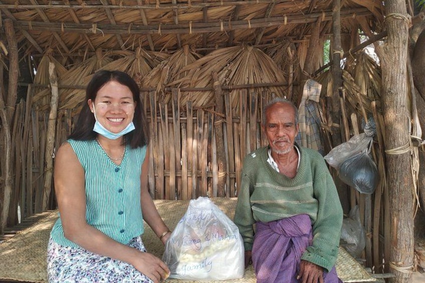 Two people sitting in a thatched hut with a plastic bag and a sack on the ground. 4