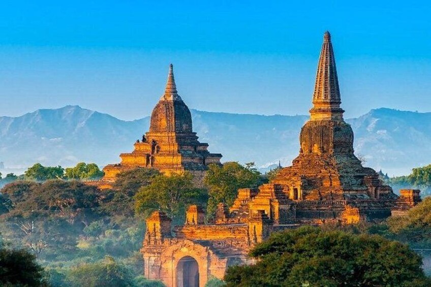 A temple complex with two prominent spires, surrounded by lush greenery and mountains in the background. 1