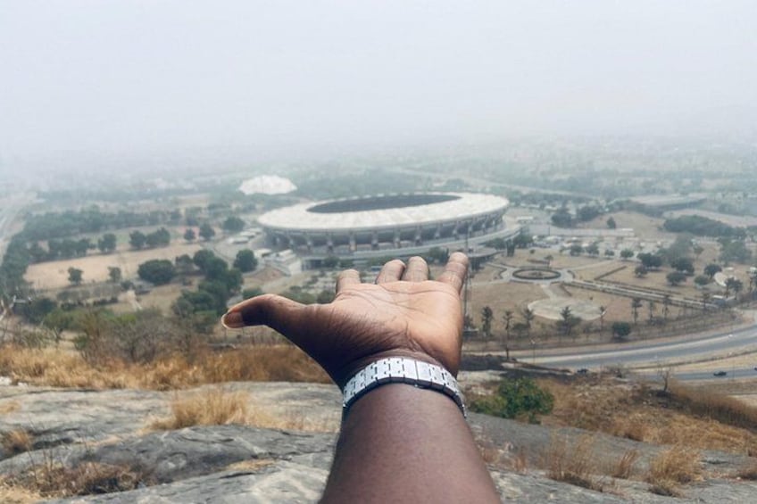 A hand with a watch, overlooking a stadium and surrounding landscape. 4