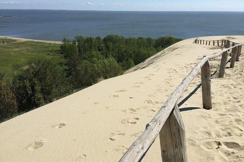 Une plage de sable avec une rambarde en bois, des empreintes de pas et une vue sur l’océan. 2