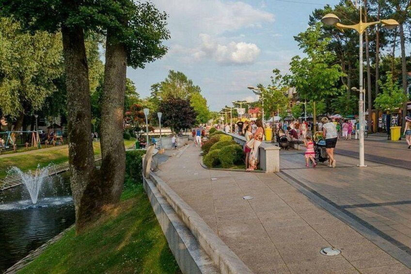 A park with a fountain, trees, a paved walkway, and people. 2