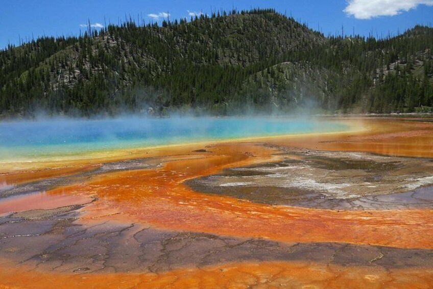 A geothermal hot spring with a gradient of colors from blue to orange, surrounded by forested hills. 4