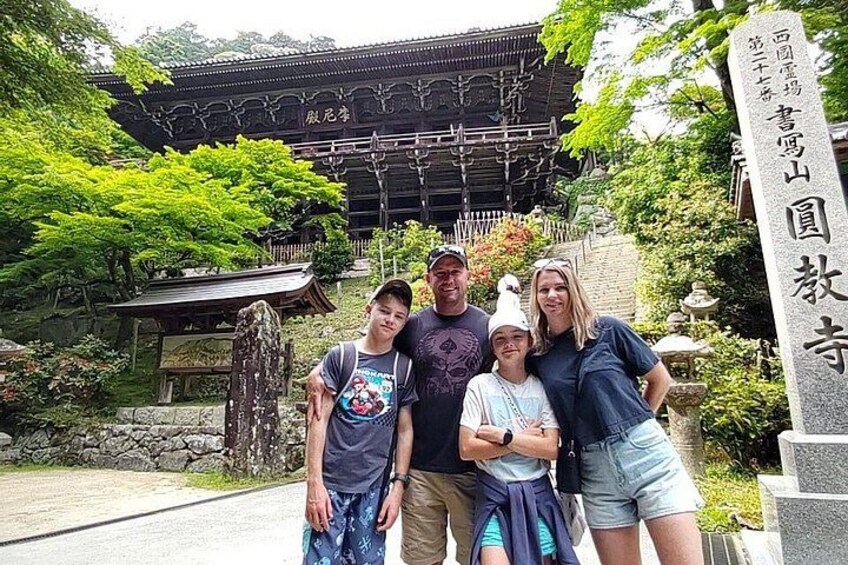 En traditionell japansk byggnad med ett stenmonument och grönska i förgrunden. 4