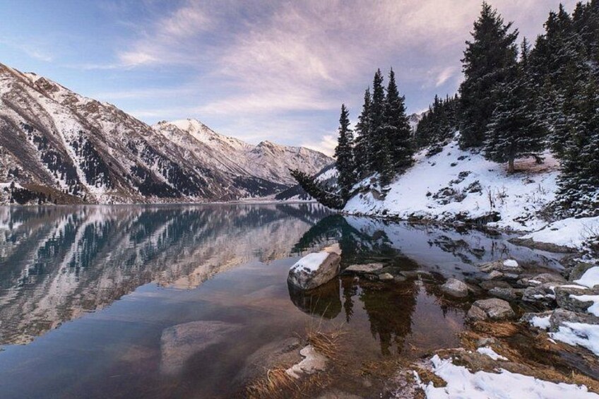 Un lac de montagne aux eaux limpides, dont les rives sont bordées de pentes enneigées et d’arbres à feuilles persistantes. 2