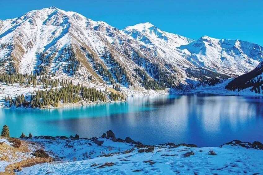 Une chaîne de montagnes enneigées, un lac aux eaux d’un bleu limpide et une zone boisée. 3