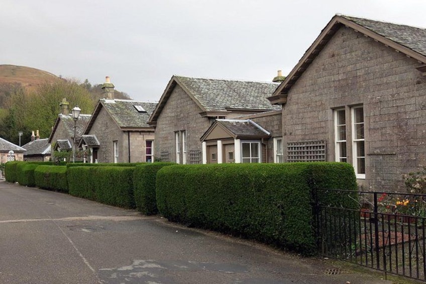 A row of stone houses with a well-maintained hedge and a metal fence. 2